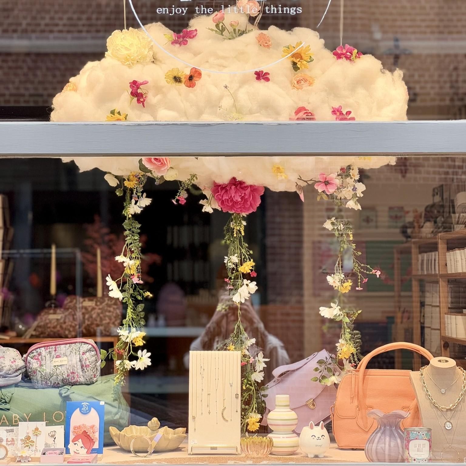 Vitrine de la boutique Mim's à Leuze-en-Hainaut décorée d’un nuage en ouate et fleurs poétiques au-dessus d’une sélection de bijoux