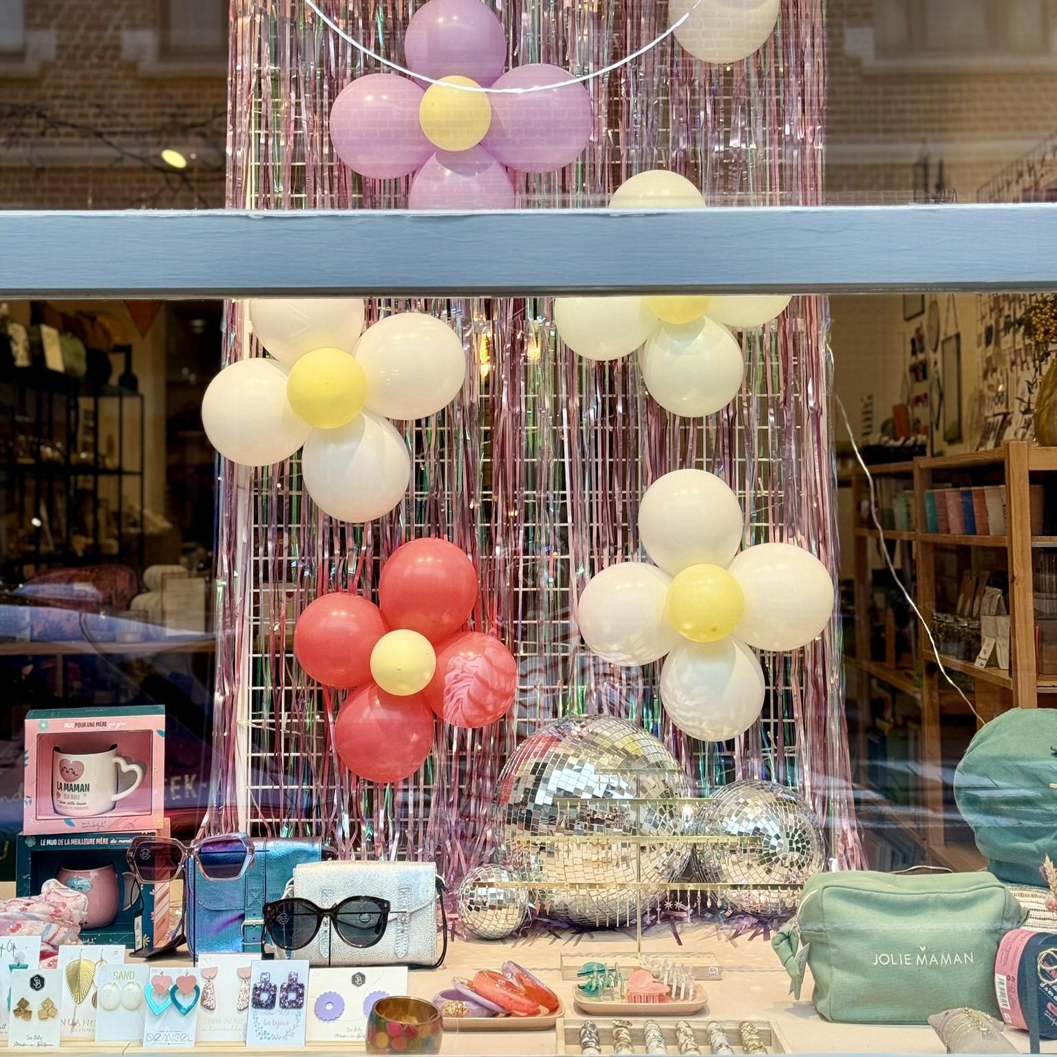 Vitrine de la boutique Mim's à Leuze-en-Hainaut avec ballons gonflables formant des fleurs, boules à facette, sacs et tasses pour la fête des mères