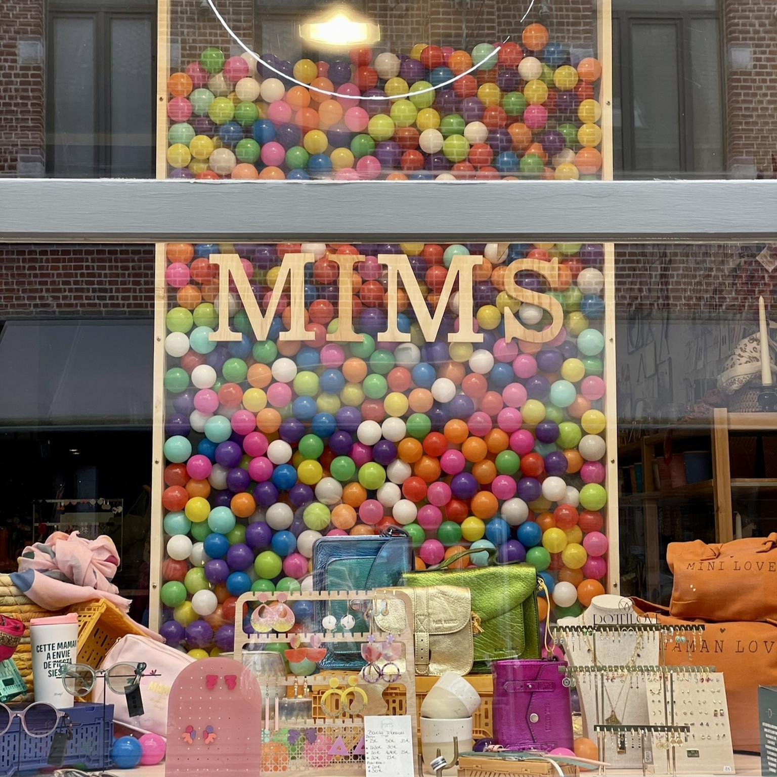 Vitrine de la boutique Mim's à Leuze-en-Hainaut avec des sacs exposés devant un mur vertical composé de centaines de balles colorées façon piscine à balles