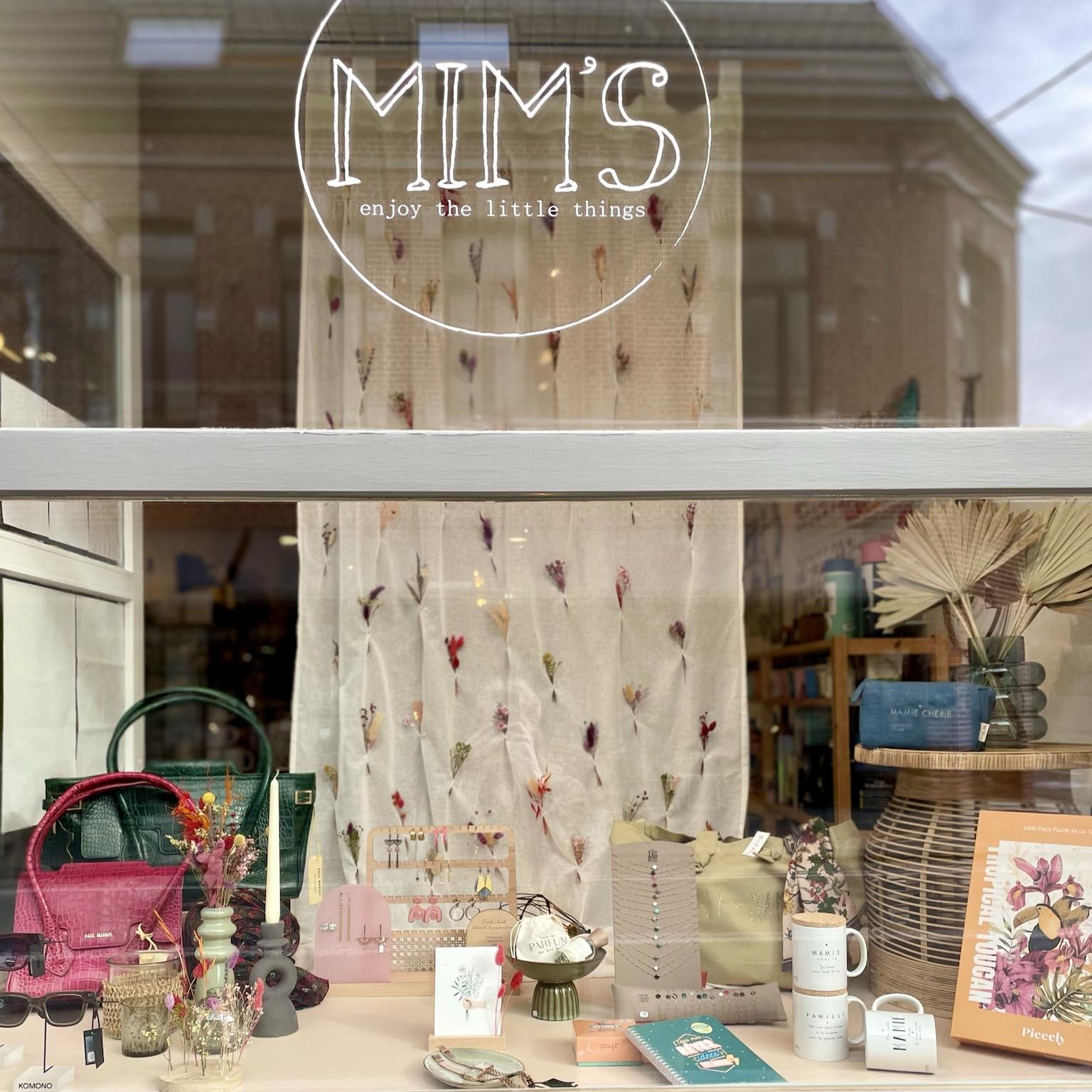 Vitrine traditionnelle de la boutique Mim's à Leuze-en-Hainaut mettant en avant des tasses, colliers et sacs dans une ambiance sobre et élégante
